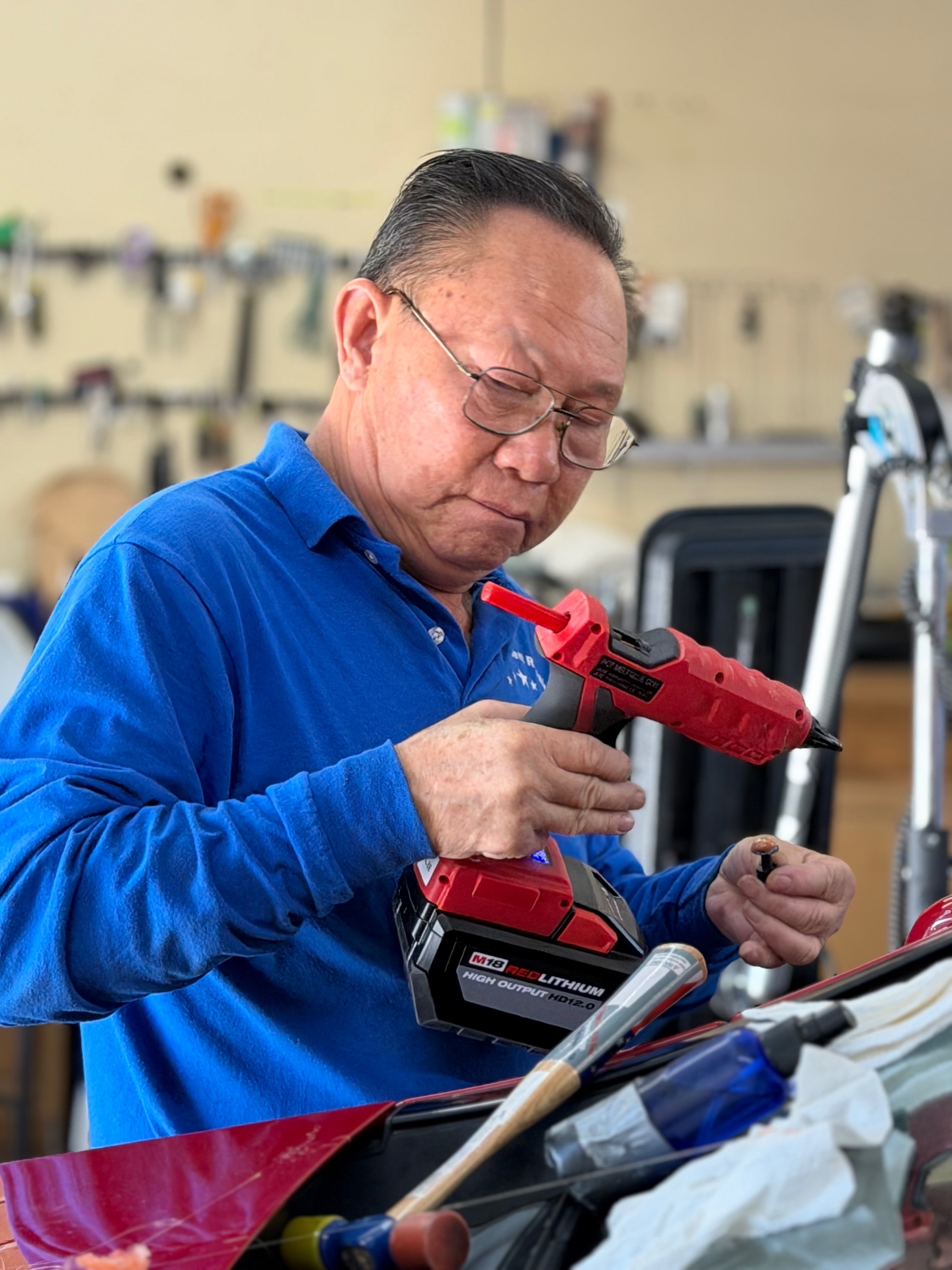 Technician holding a glue gun and a dent pull tab while working on a red vehicle panel